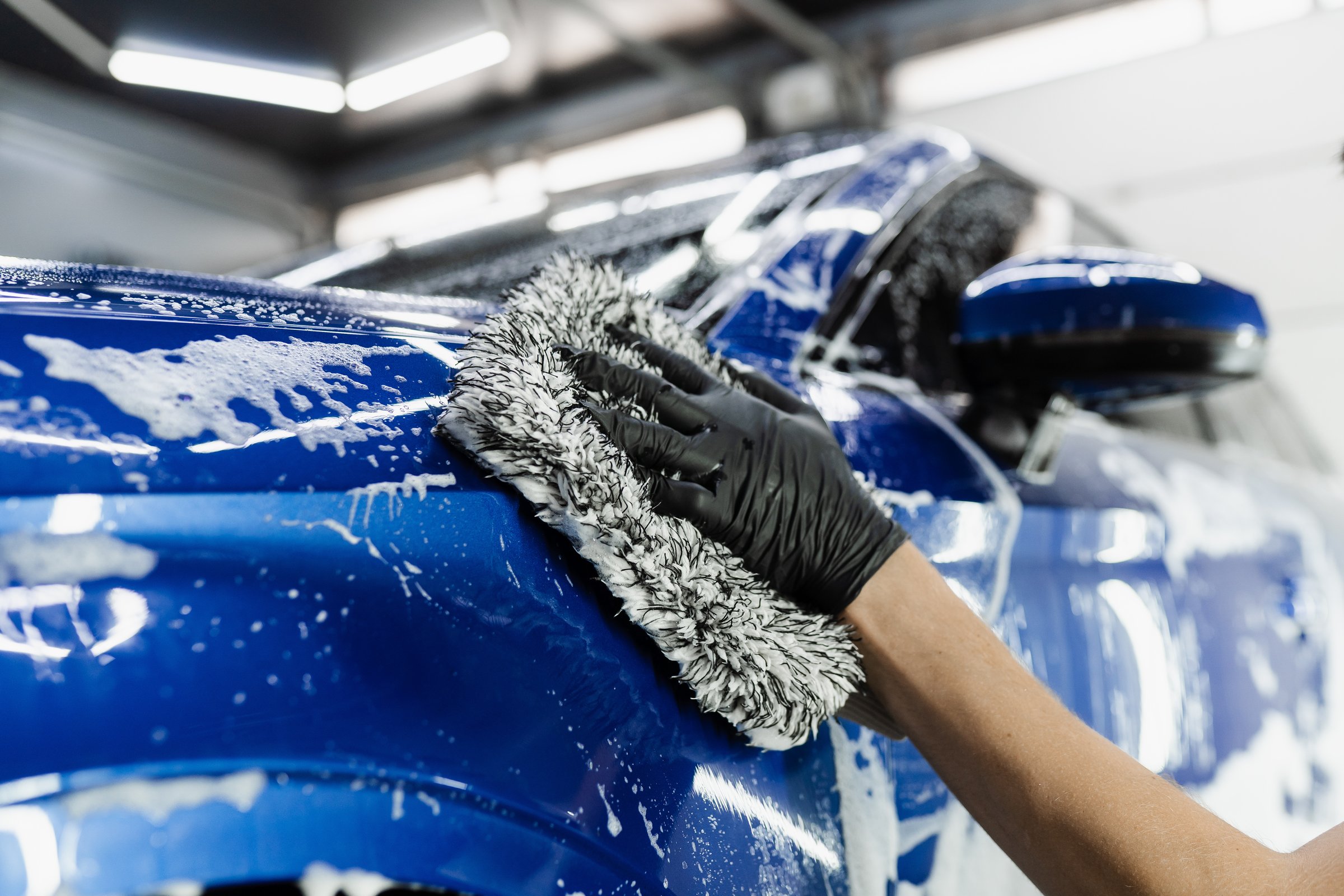 Professional hand washing microfiber glove on car body during auto detailing service
